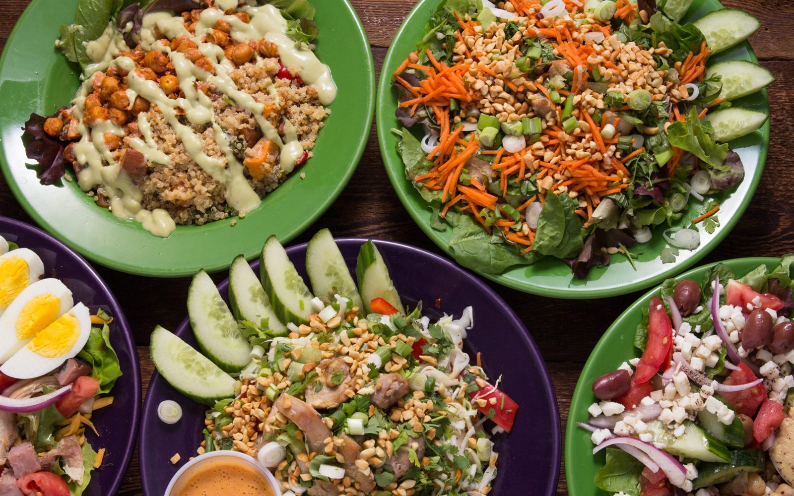 Four colorful salad bowls on a wooden table, seen from above