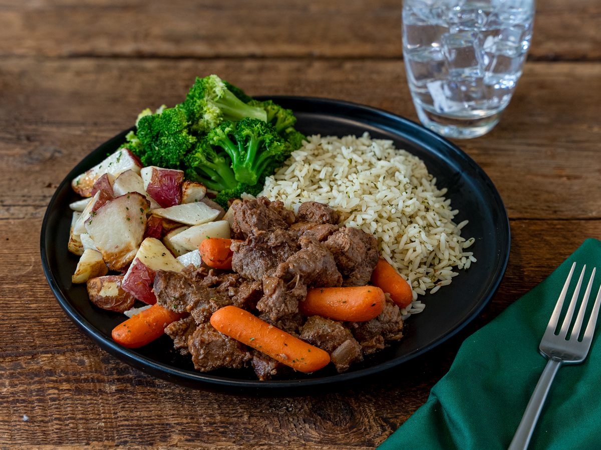 A frozen-meal dinner plated: beef tips, roasted potatoes, carrots, broccoli and rice